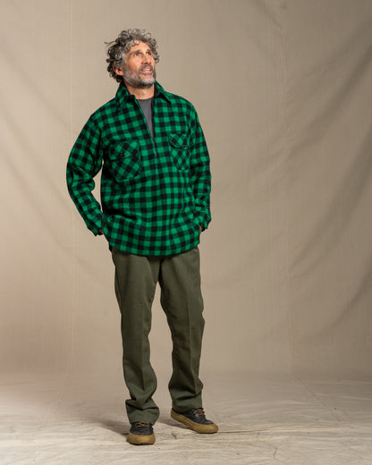 Man wearing a green plaid shirt and green pants against a beige background
