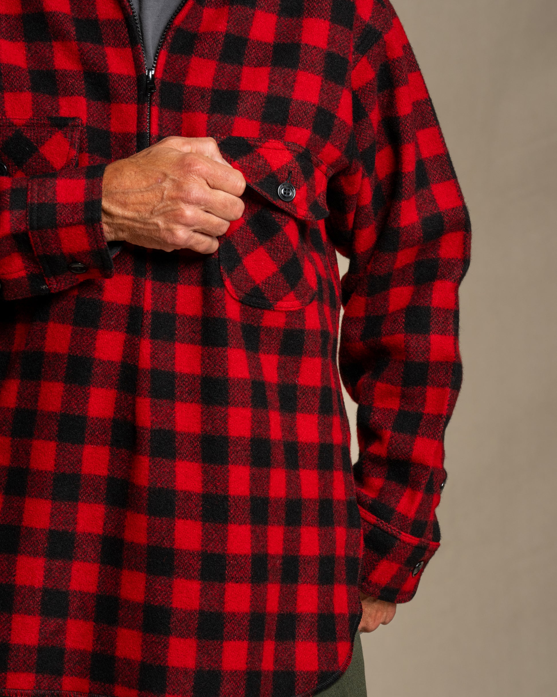 Man wearing a red and black checkered half zip wool shirt against a beige background