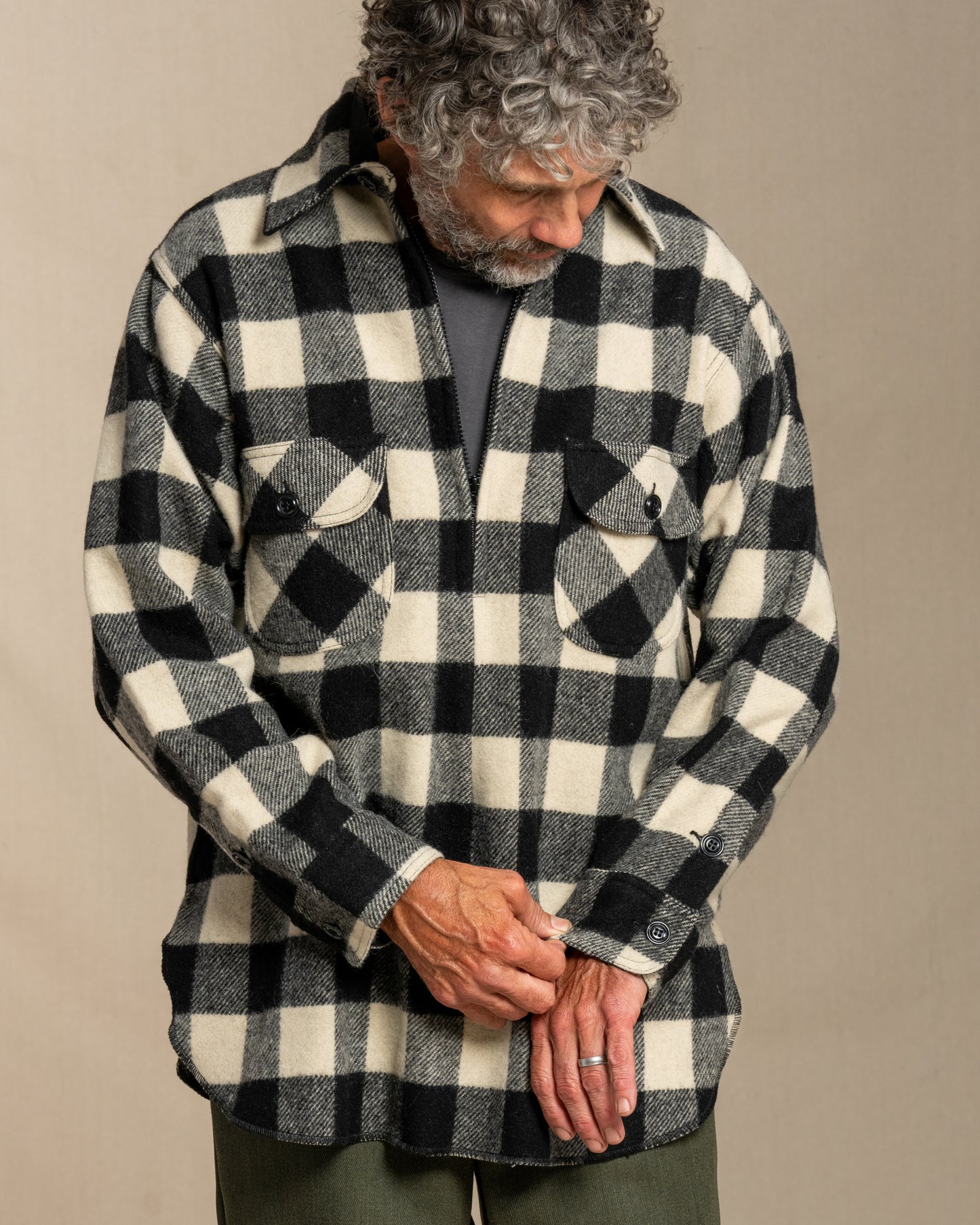 Man wearing a black and white checkered half zip wool shirt with green pants against a plain background