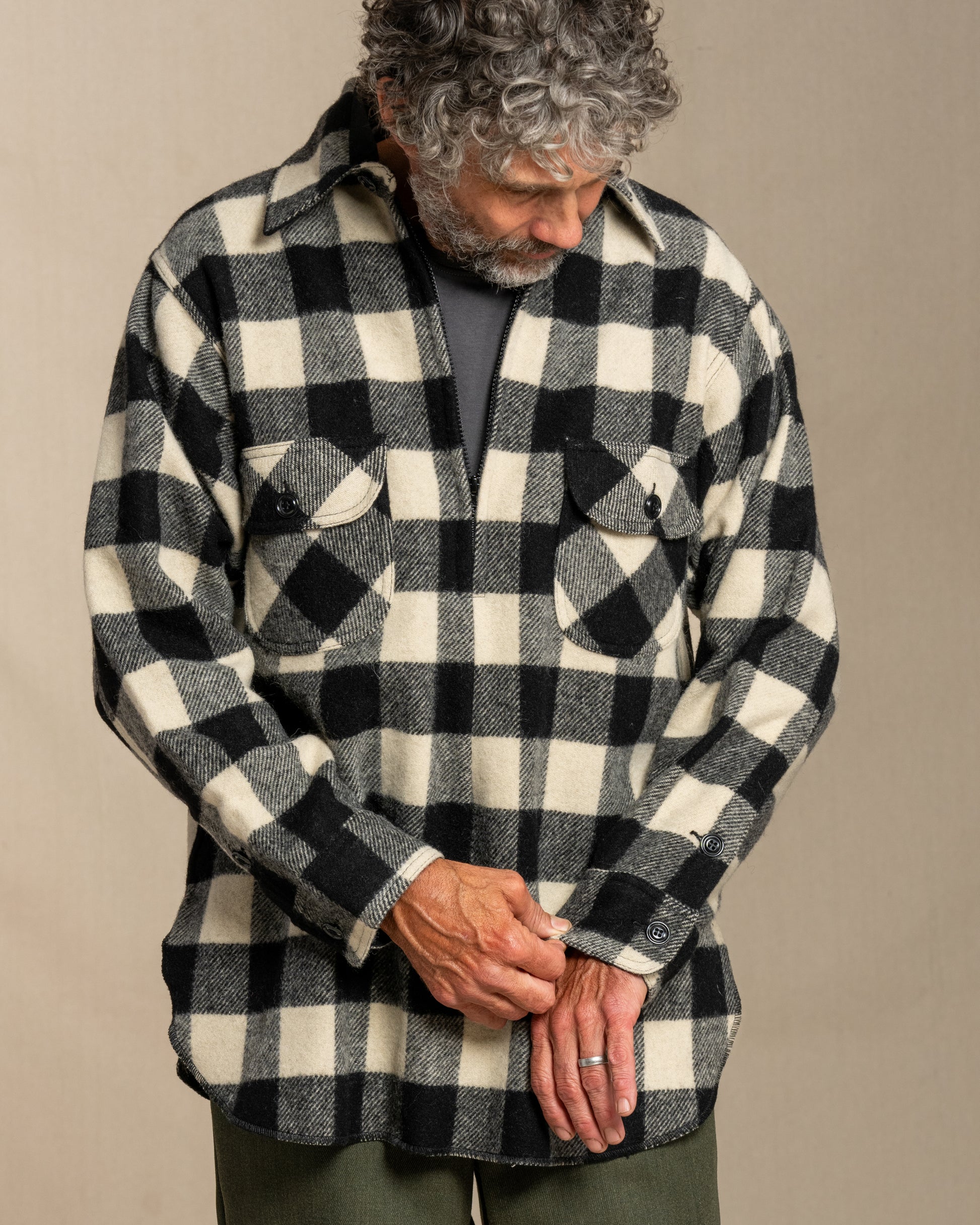 Man wearing a black and white checkered half zip wool shirt with green pants against a plain background