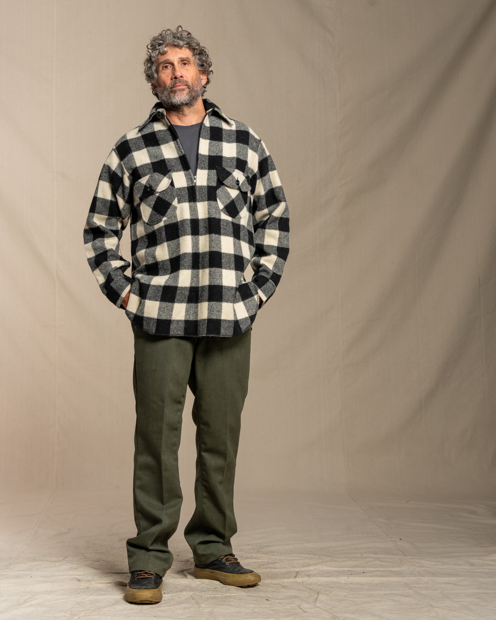 Man wearing a black and white checkered shirt with green pants against a plain background