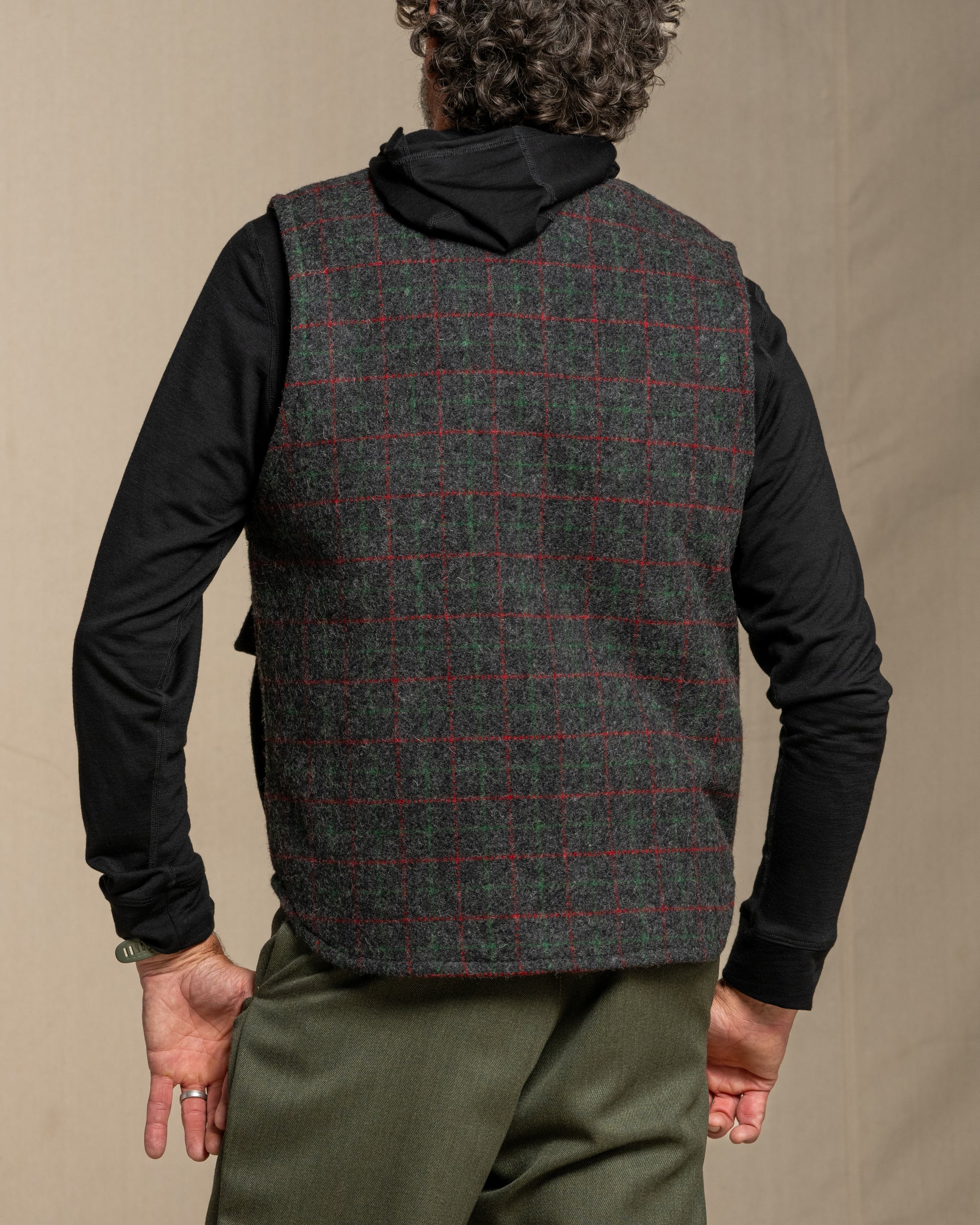 Person wearing a plaid vest over a black shirt with a beige background