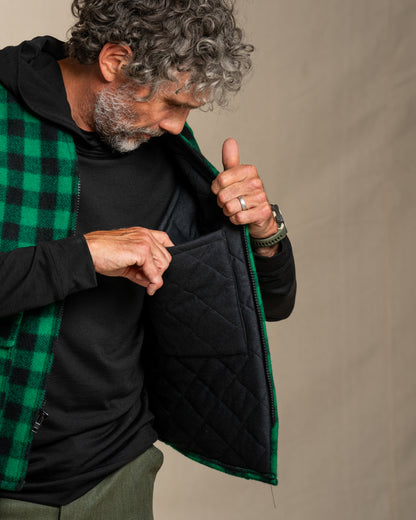 Man wearing a green and black checkered wool vest with a black quilted lining against a beige background.