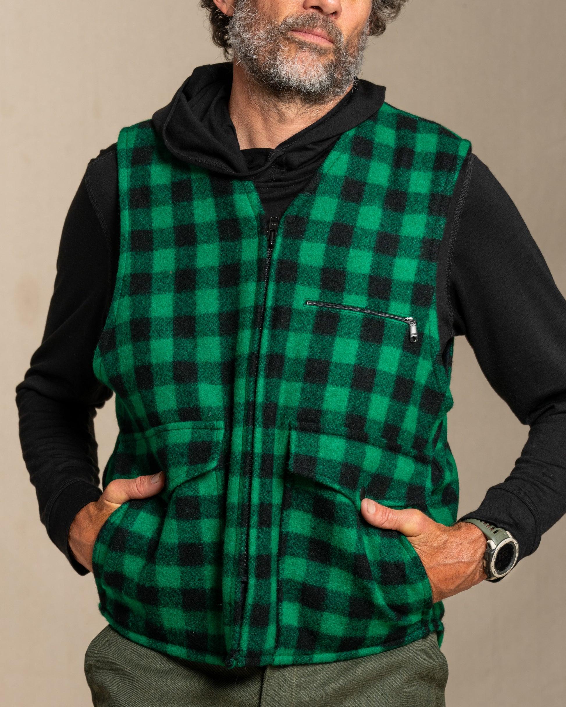 Man wearing a green and black checkered wool vest against a beige background