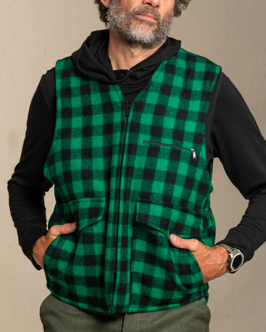 Man wearing a green and black checkered wool vest against a beige background
