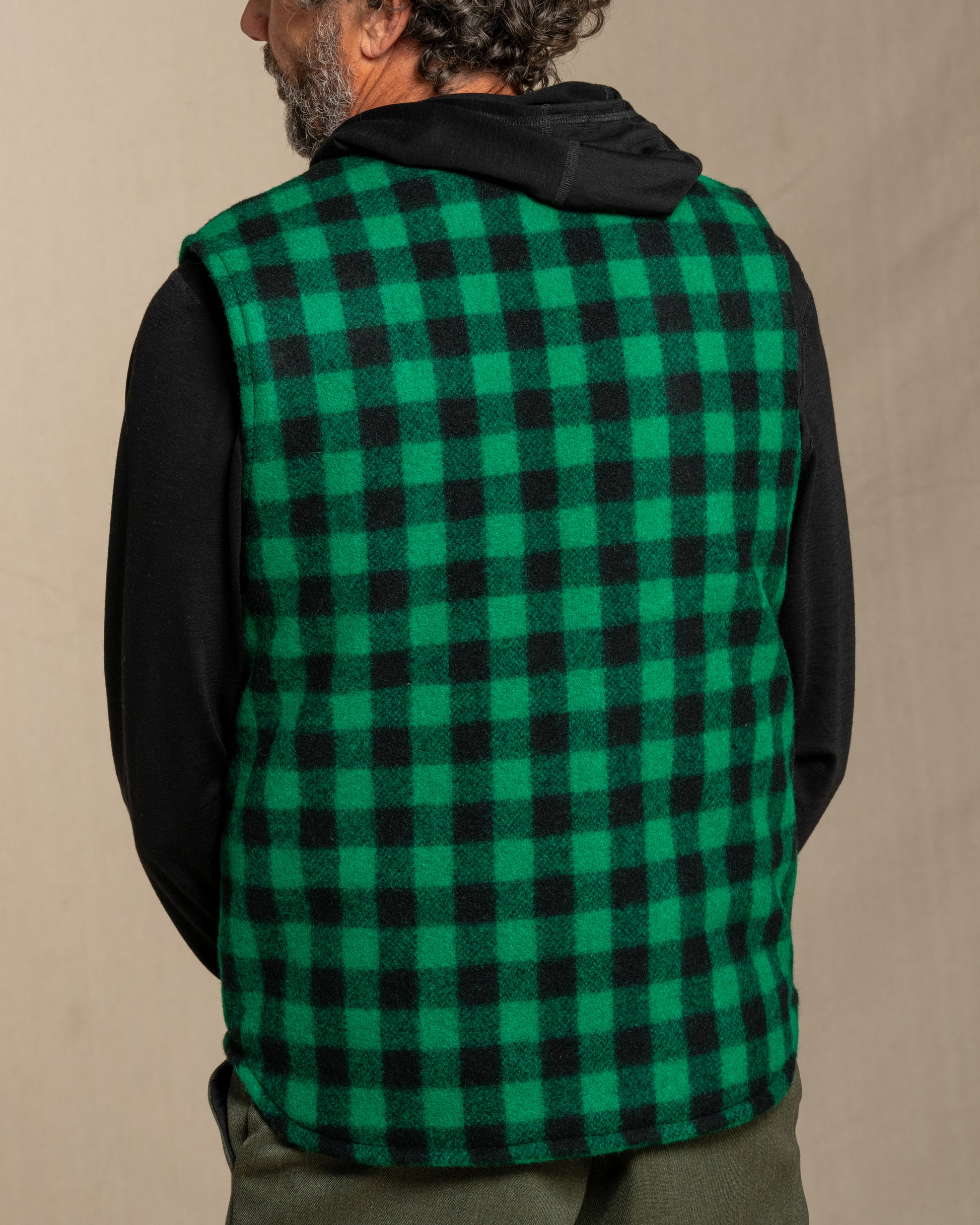 Man wearing a green and black checkered wool vest against a beige background
