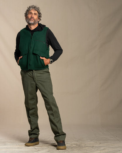 Man wearing a green wool vest over a black merino wool shirt with green wool pants against a plain background