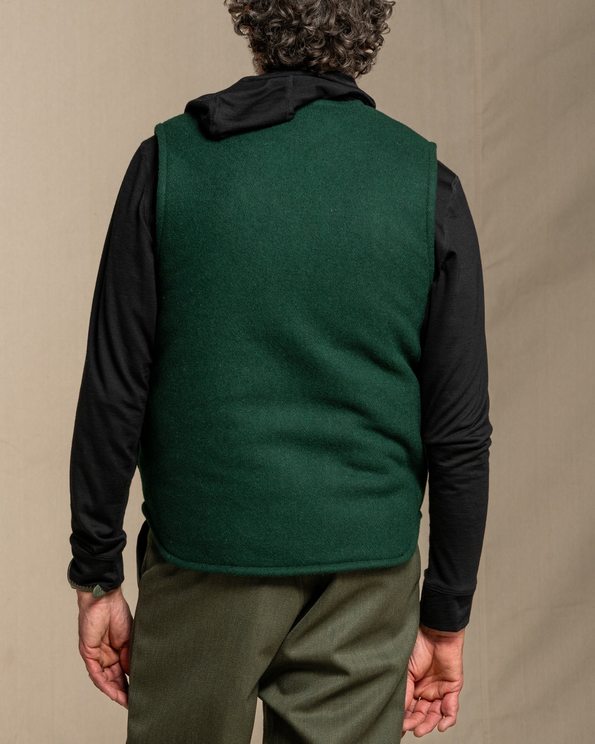 Person wearing a green wool vest over a black shirt with a beige background