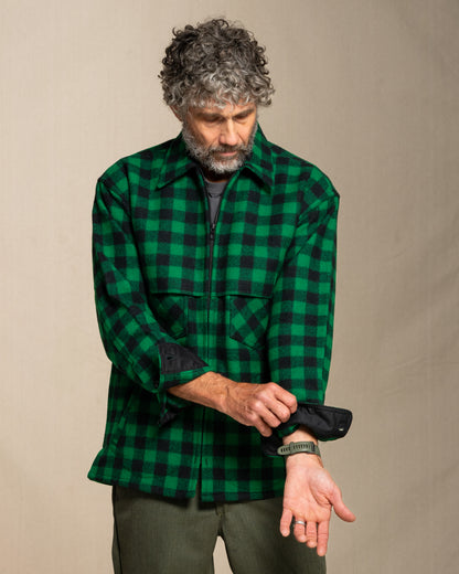 Man wearing a green and black plaid jac shirt against a beige background