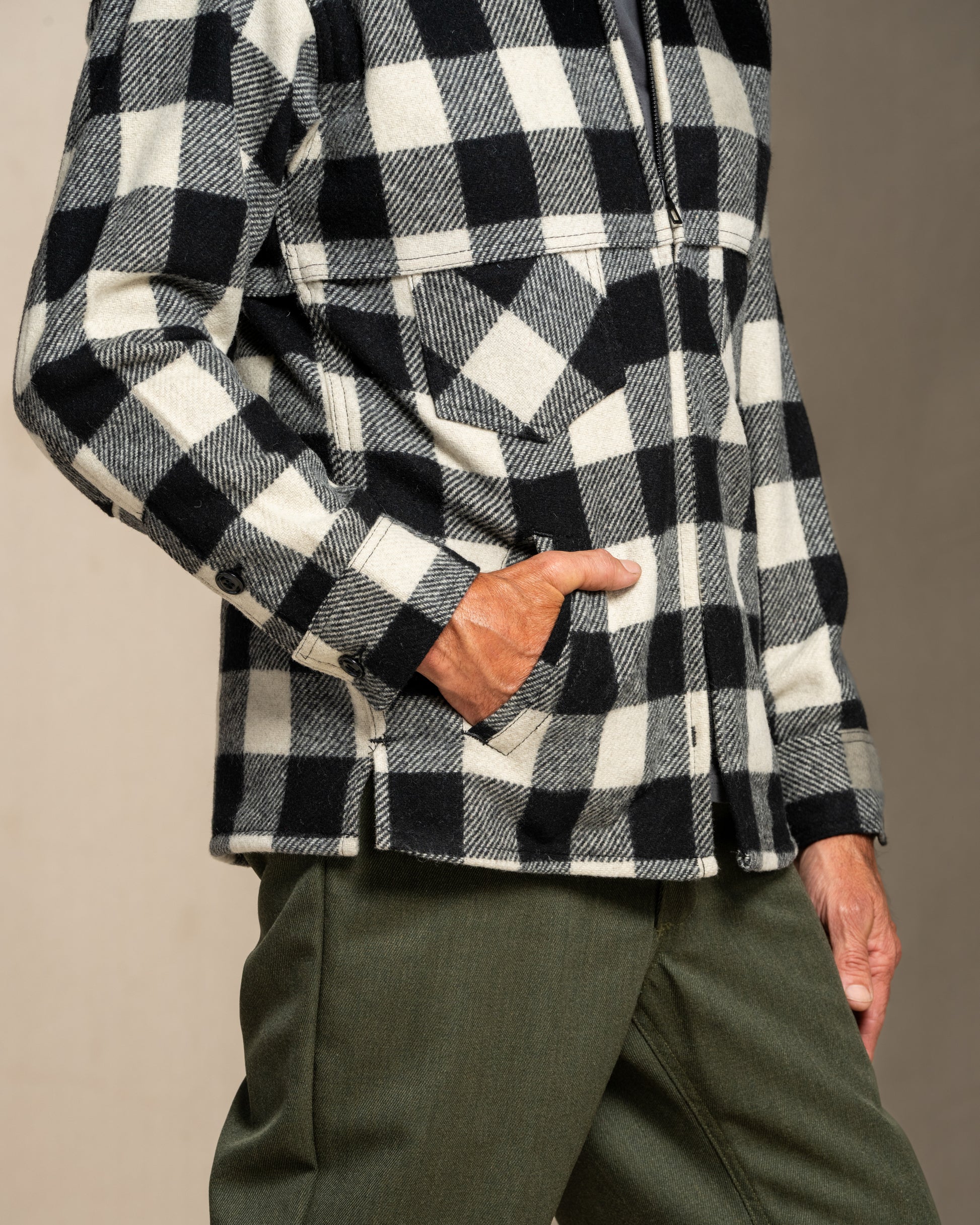 Person wearing a black and white checkered wool jacket with green pants on a neutral background