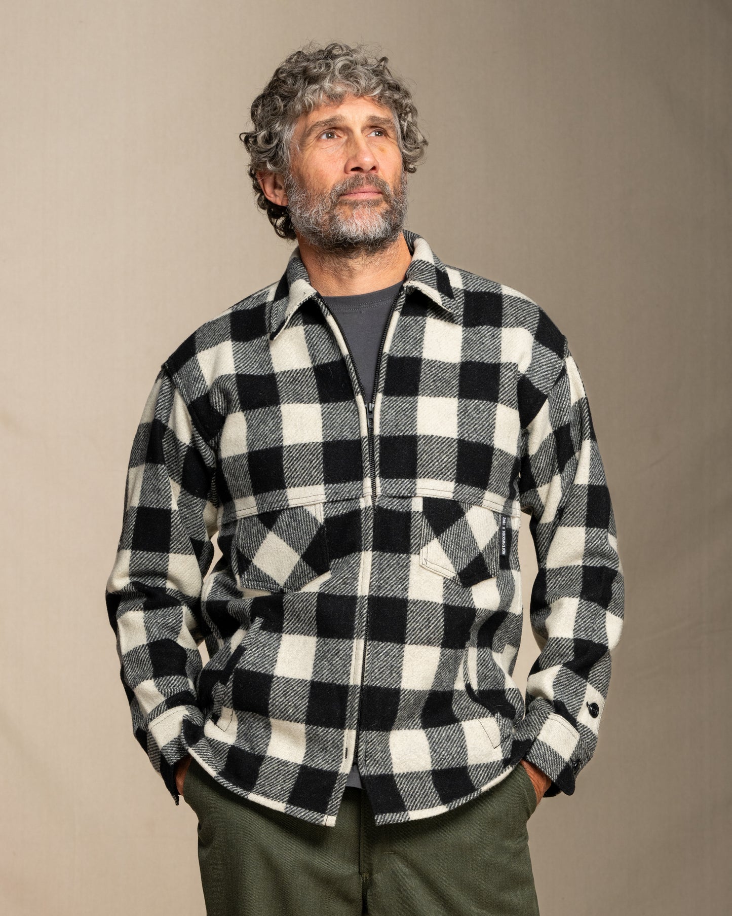 Man wearing a black and white checkered wool coat and green pants against a plain background