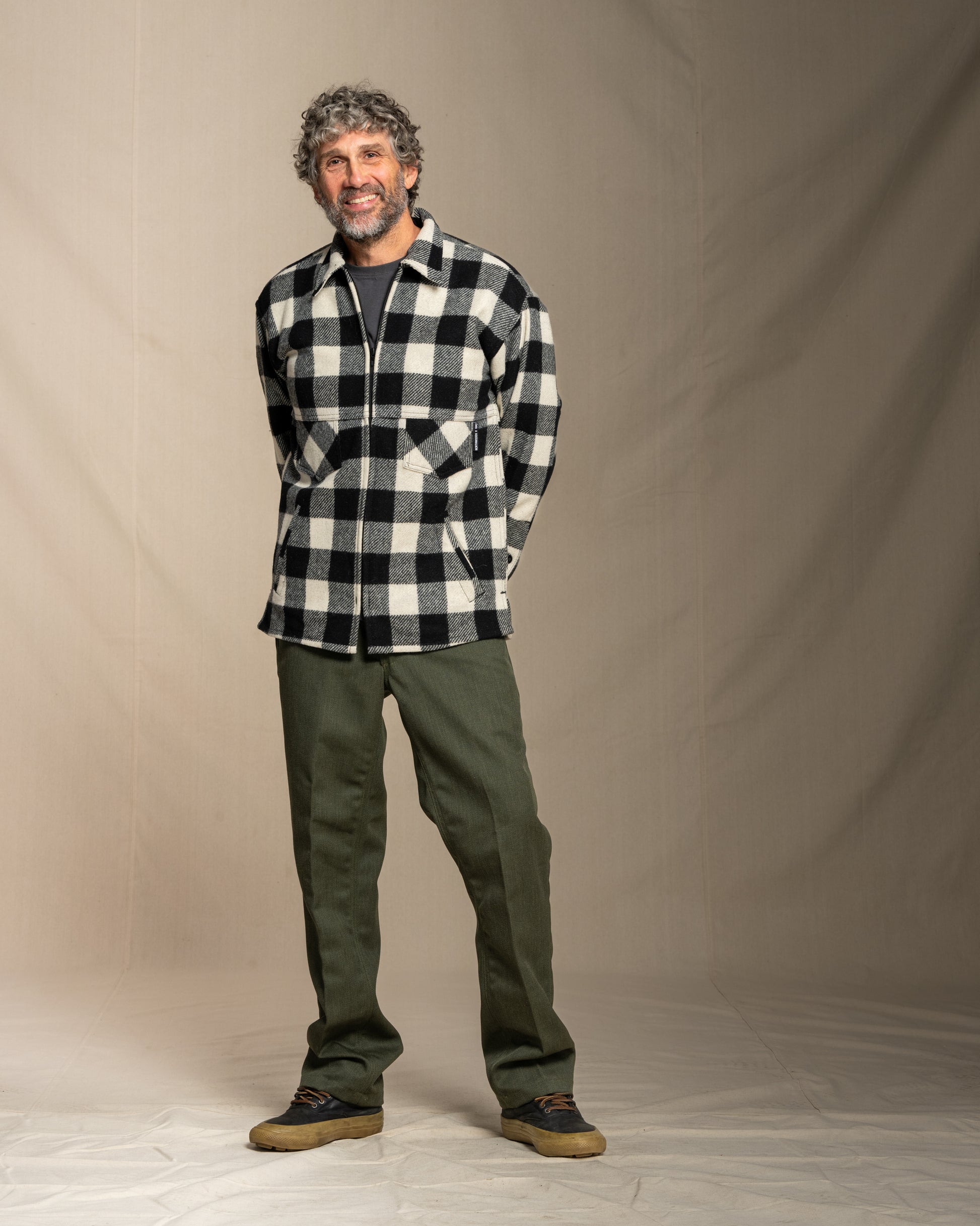 Man wearing a black and white checkered wool coat and green pants against a plain background