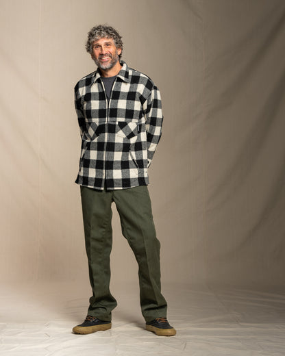 Man wearing a black and white checkered wool coat and green pants against a plain background