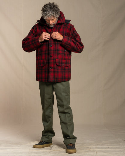Man wearing a red plaid jacket and green pants against a beige background