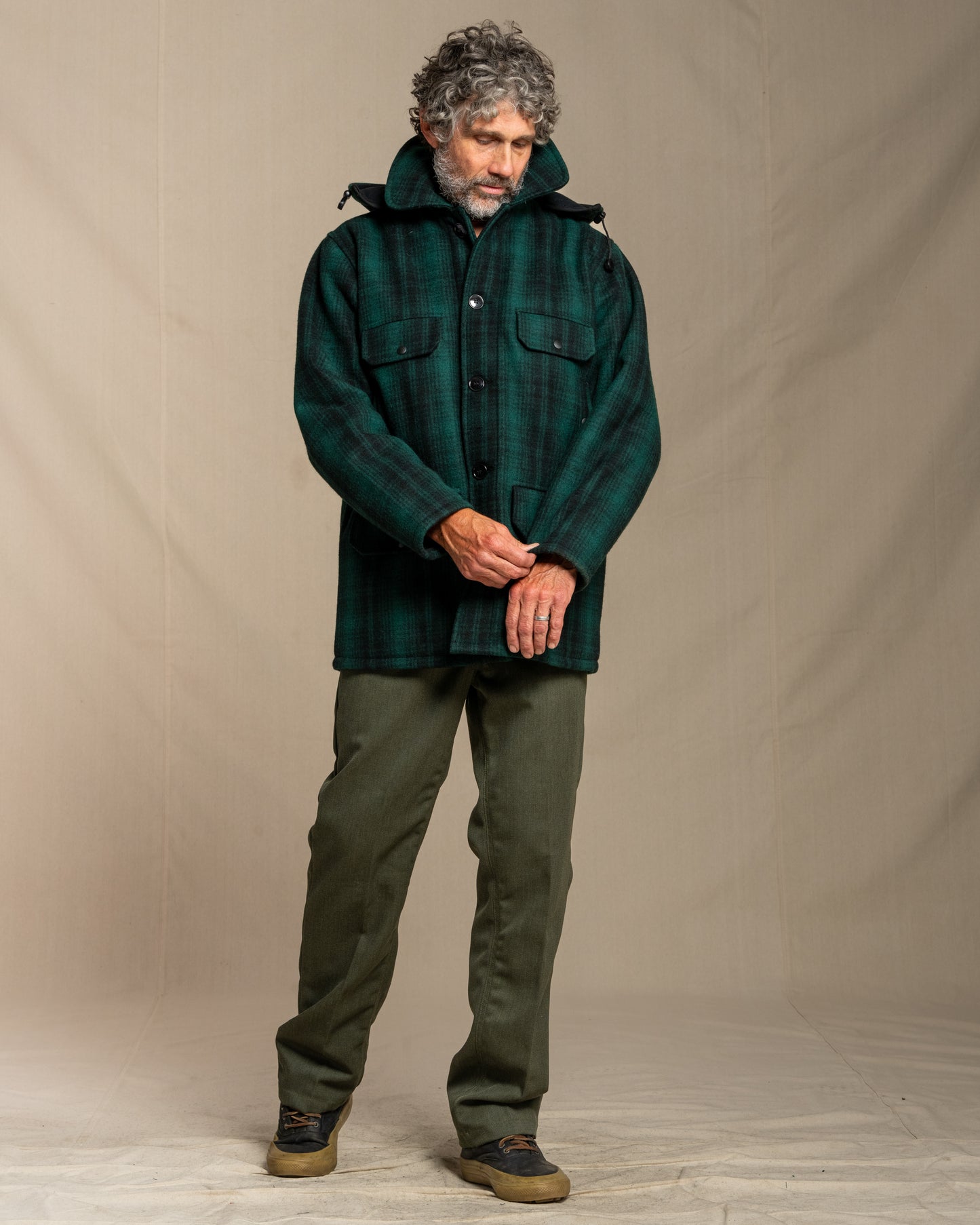Man wearing a green plaid wool jacket and pants against a beige background