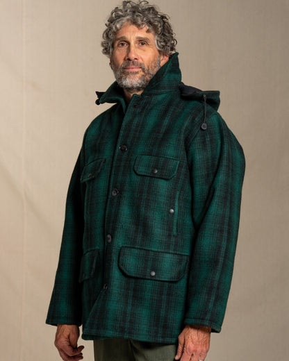 Man wearing a green plaid wool jacket and pants against a beige background