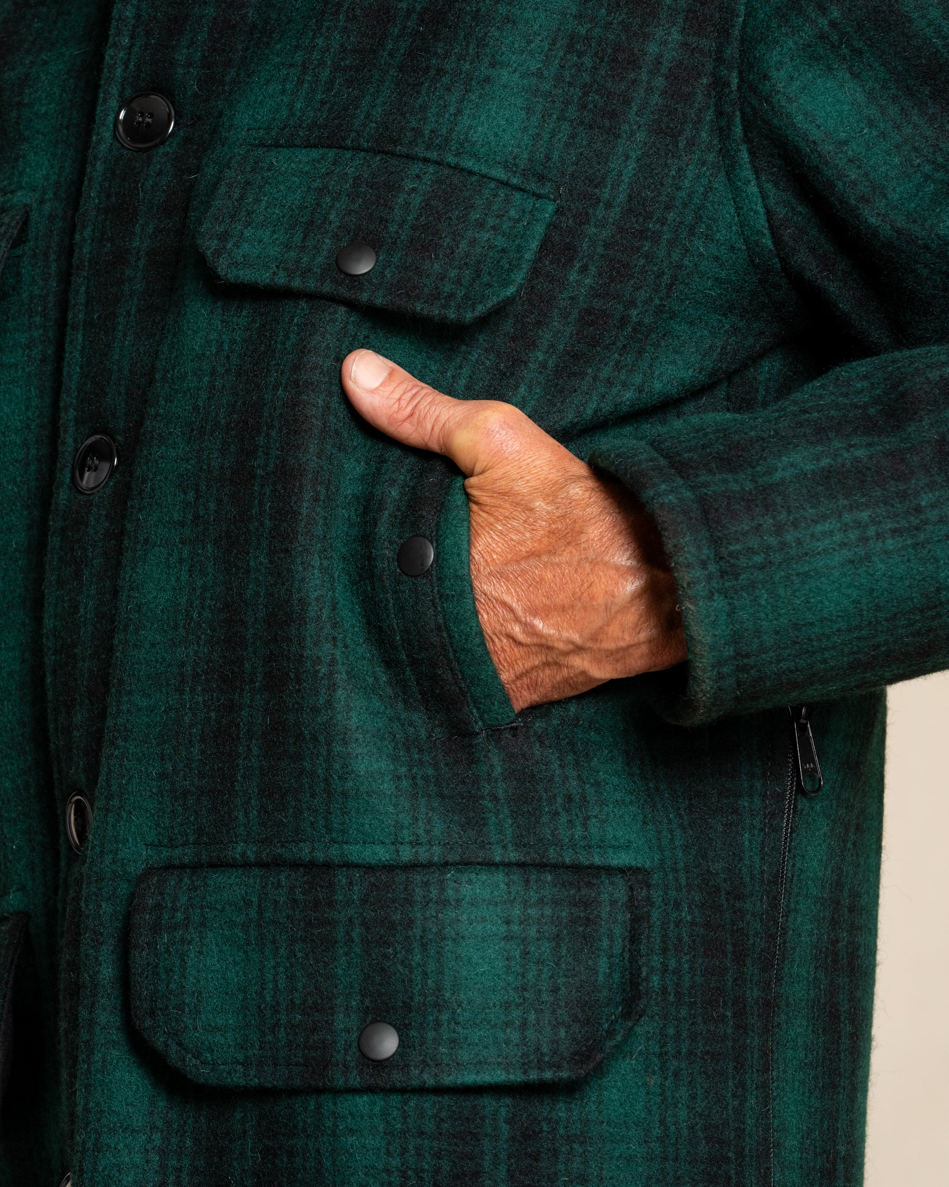 Close-up of a person wearing a green plaid jacket with a hand in the pocket.
