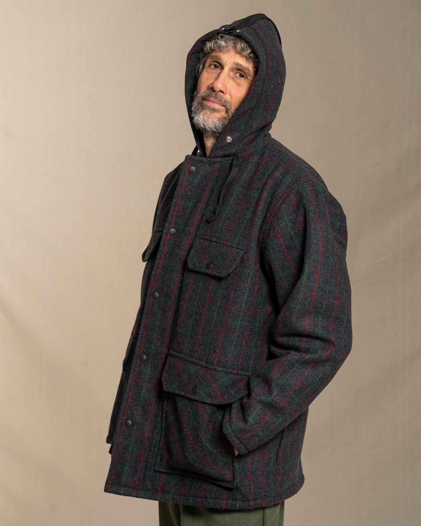 Man wearing a dark plaid coat with a hood against a beige background