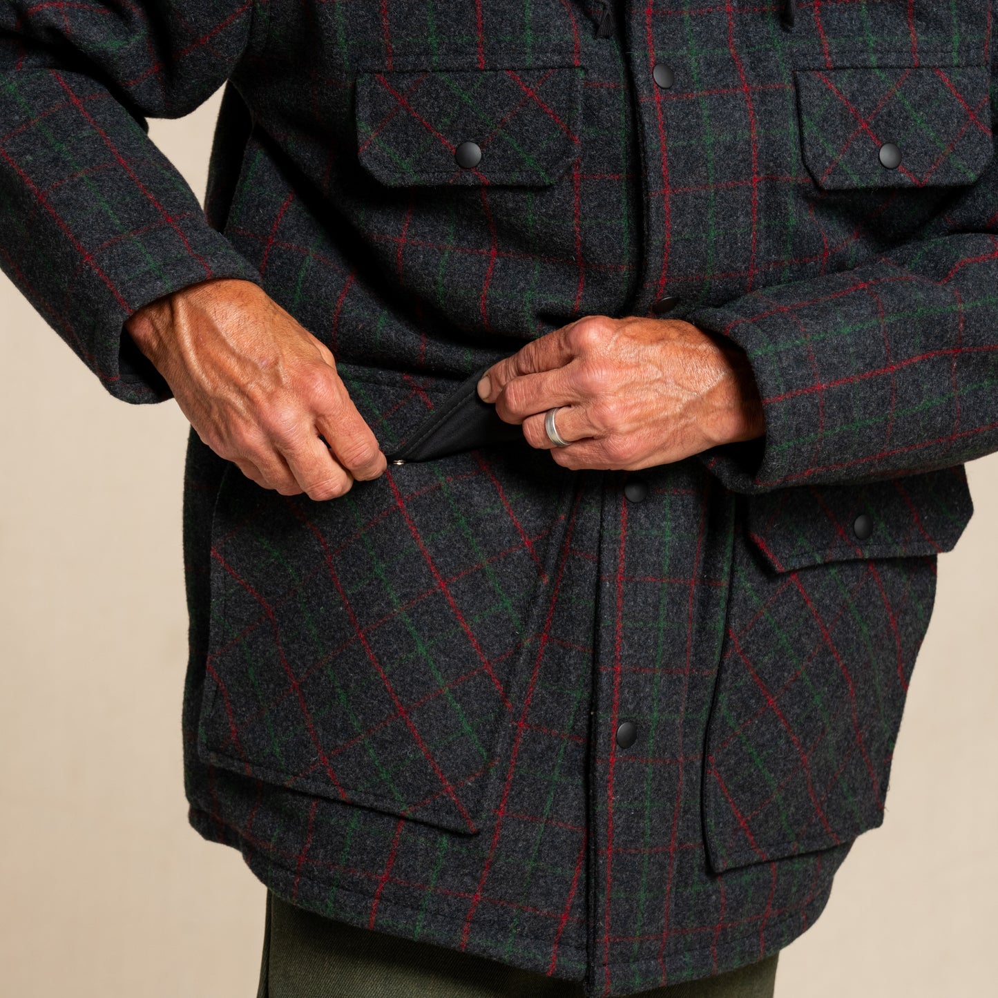 Person wearing a dark green and red plaid jacket on a beige background