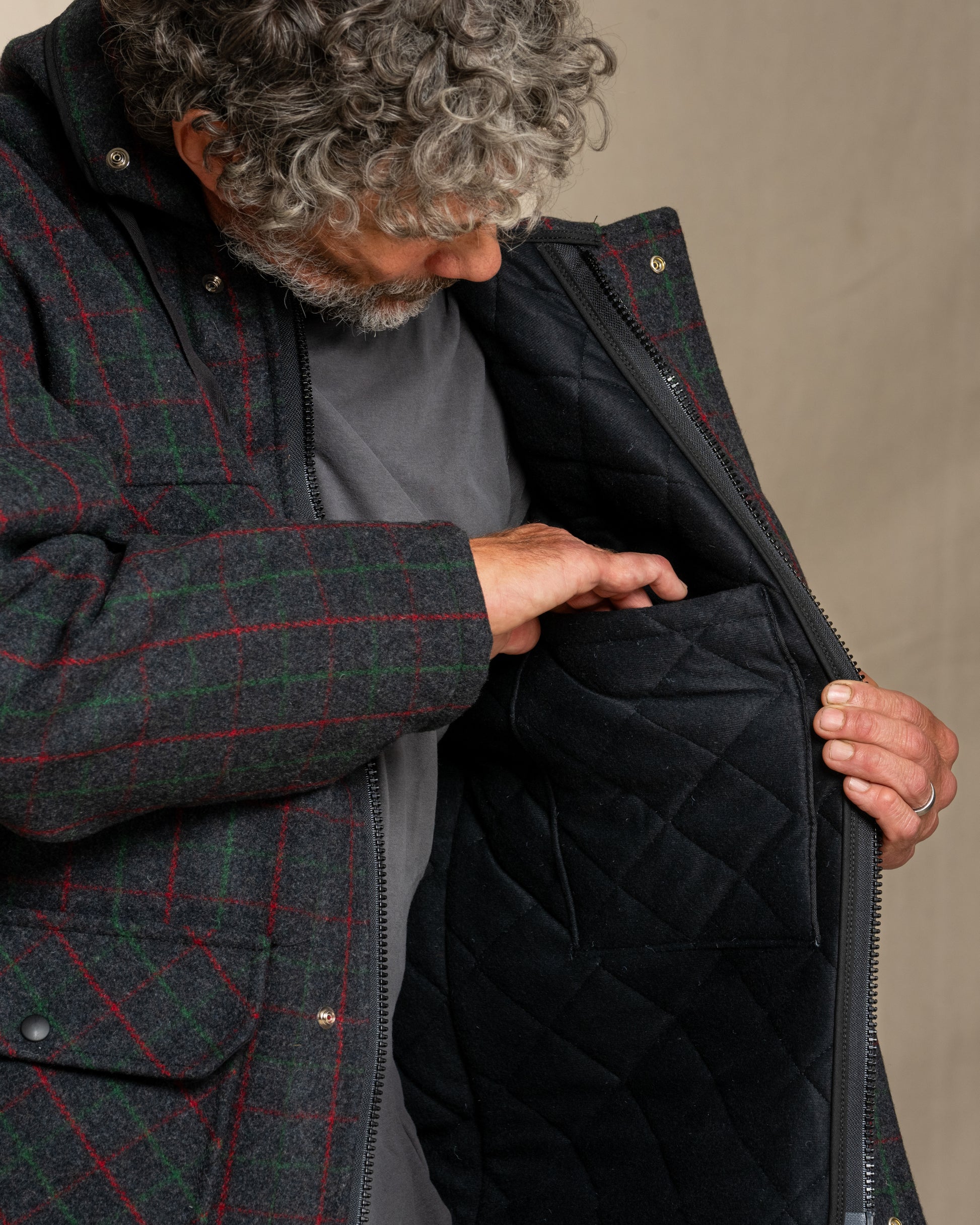 Person wearing a dark green checkered jacket with a quilted black lining, opening the jacket.