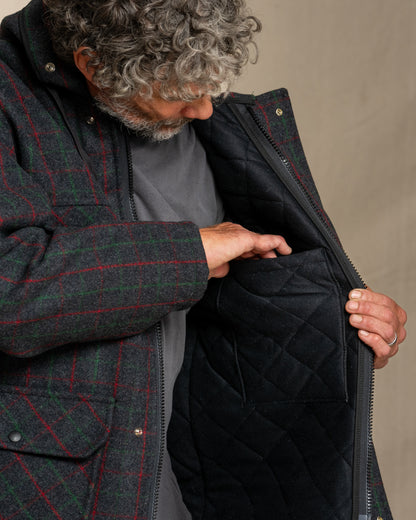 Person wearing a dark green checkered jacket with a quilted black lining, opening the jacket.