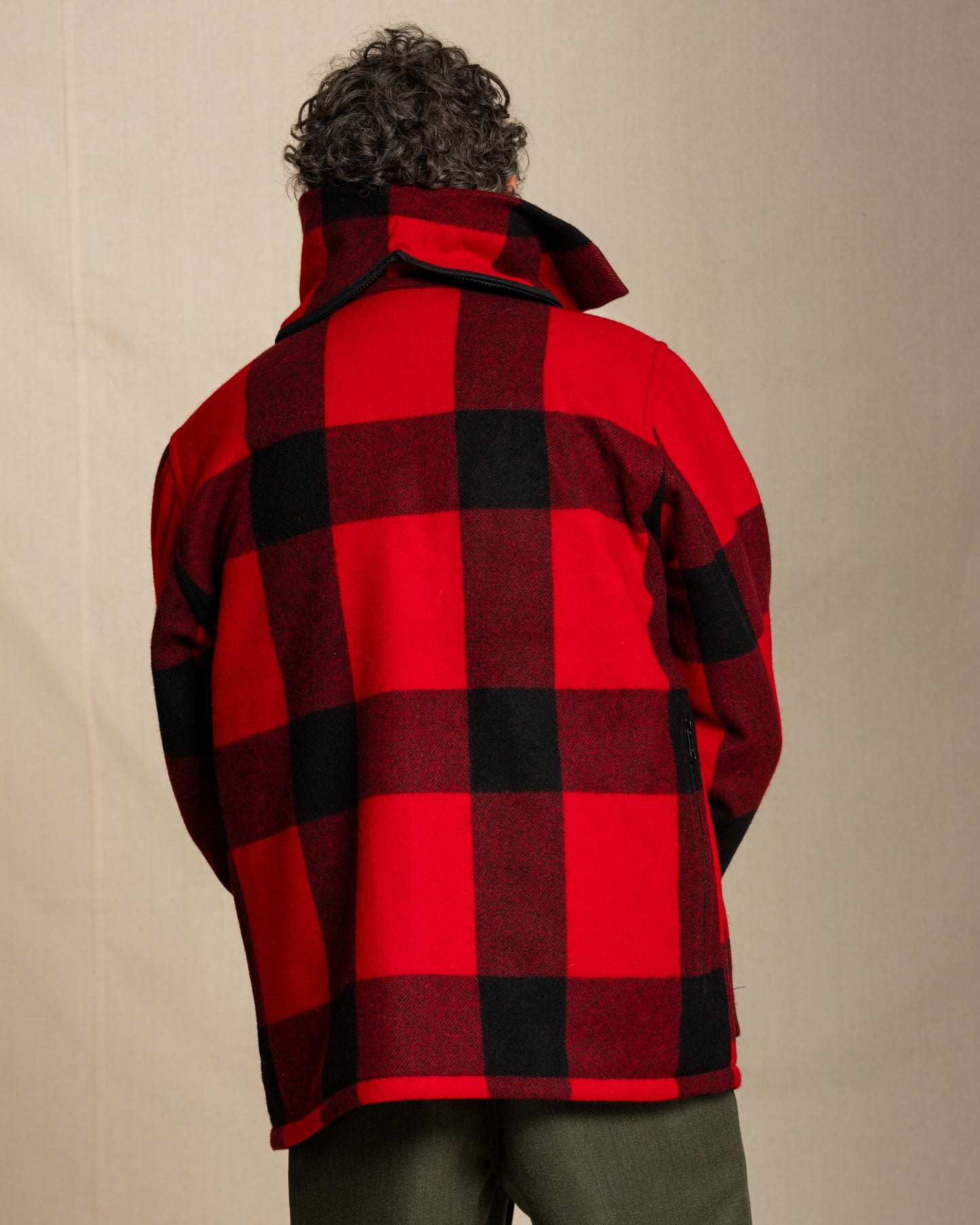 Person wearing a red and black checkered jacket against a beige background