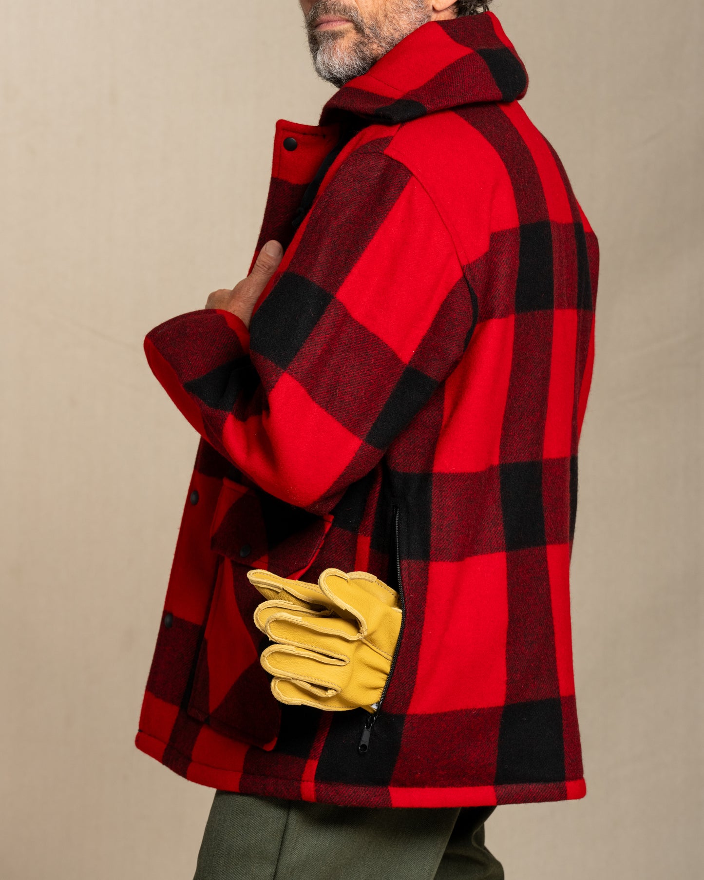 Person wearing a red and black checkered coat with yellow gloves against a beige background