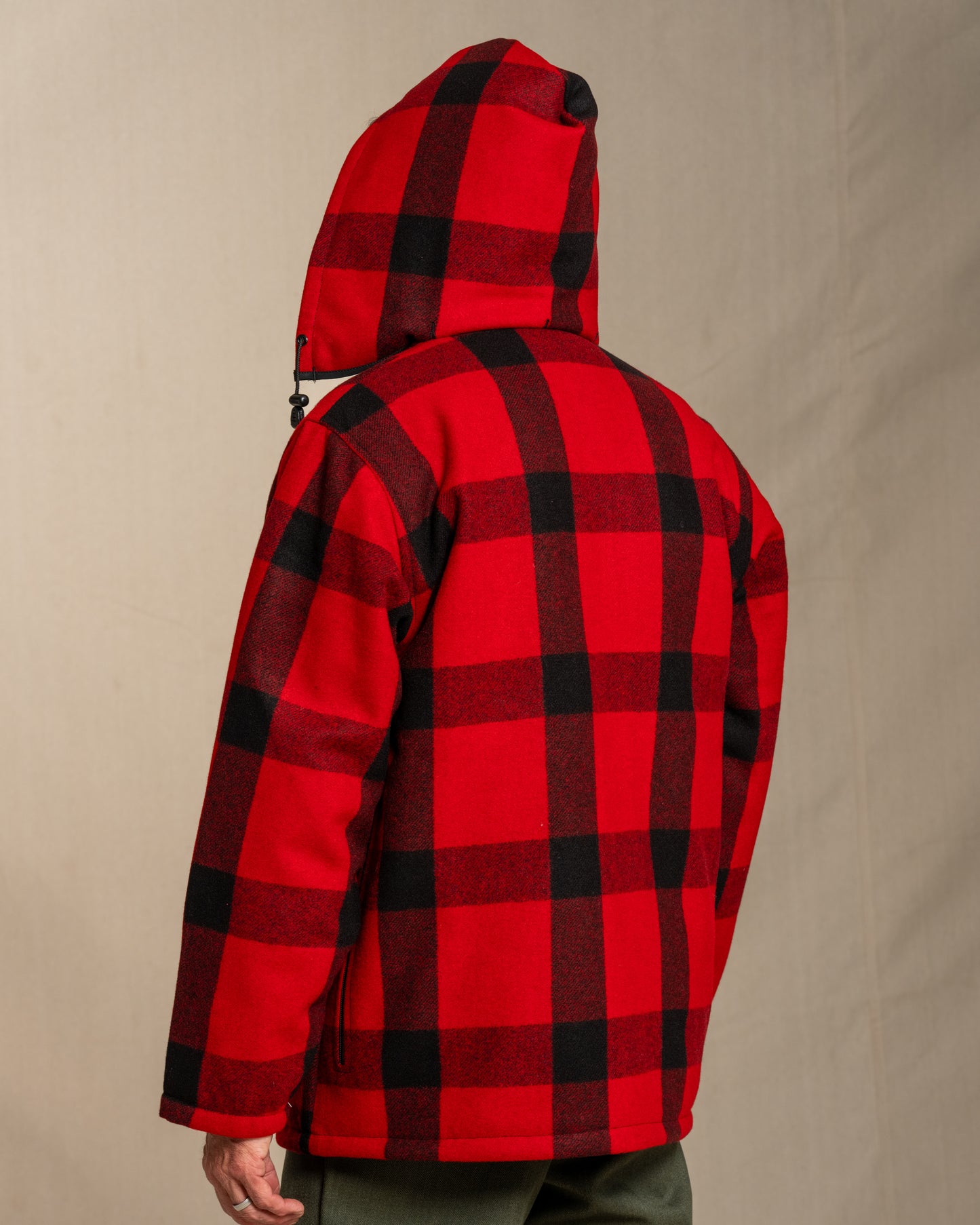 Person wearing a red and black plaid wool mackinaw jacket against a beige background