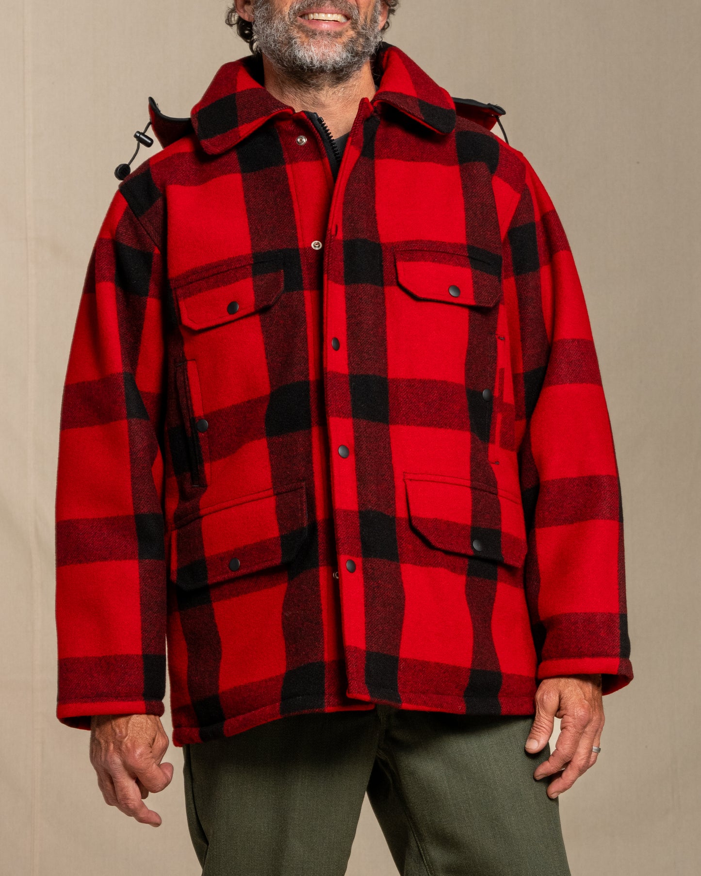 Person wearing a red and black plaid wool mackinaw jacket against a beige background