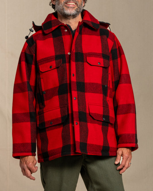 Person wearing a red and black plaid wool mackinaw jacket against a beige background
