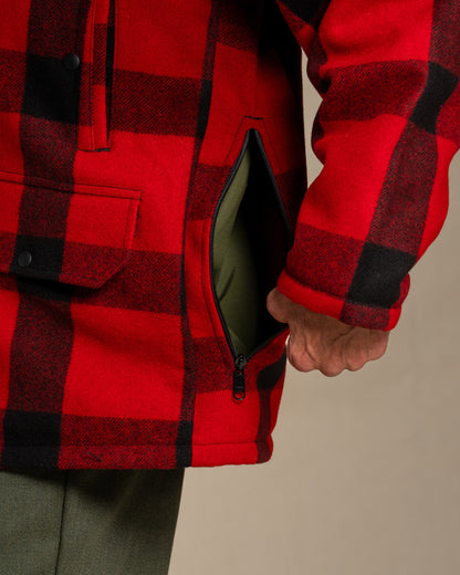 Red and black checkered jacket with a hand interacting with the zipper on a neutral background