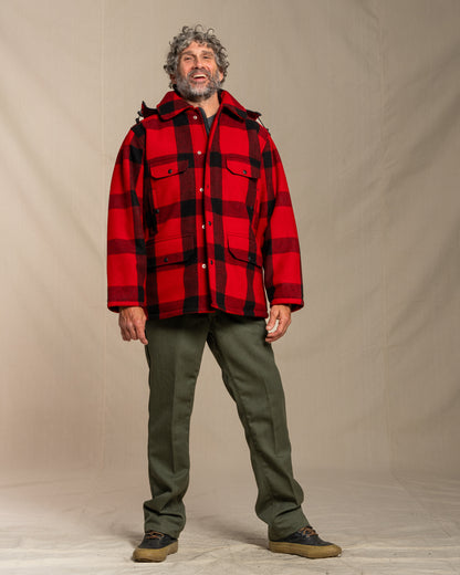 Man wearing a red and black plaid mackinaw wool jacket over a black shirt, standing against a plain background