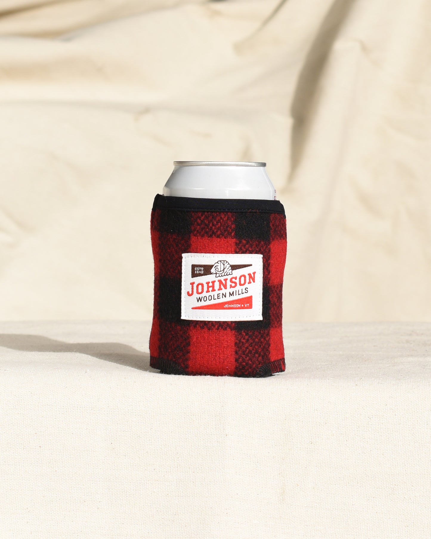 Red and black wool plaid can cooler with a white label on a beige background