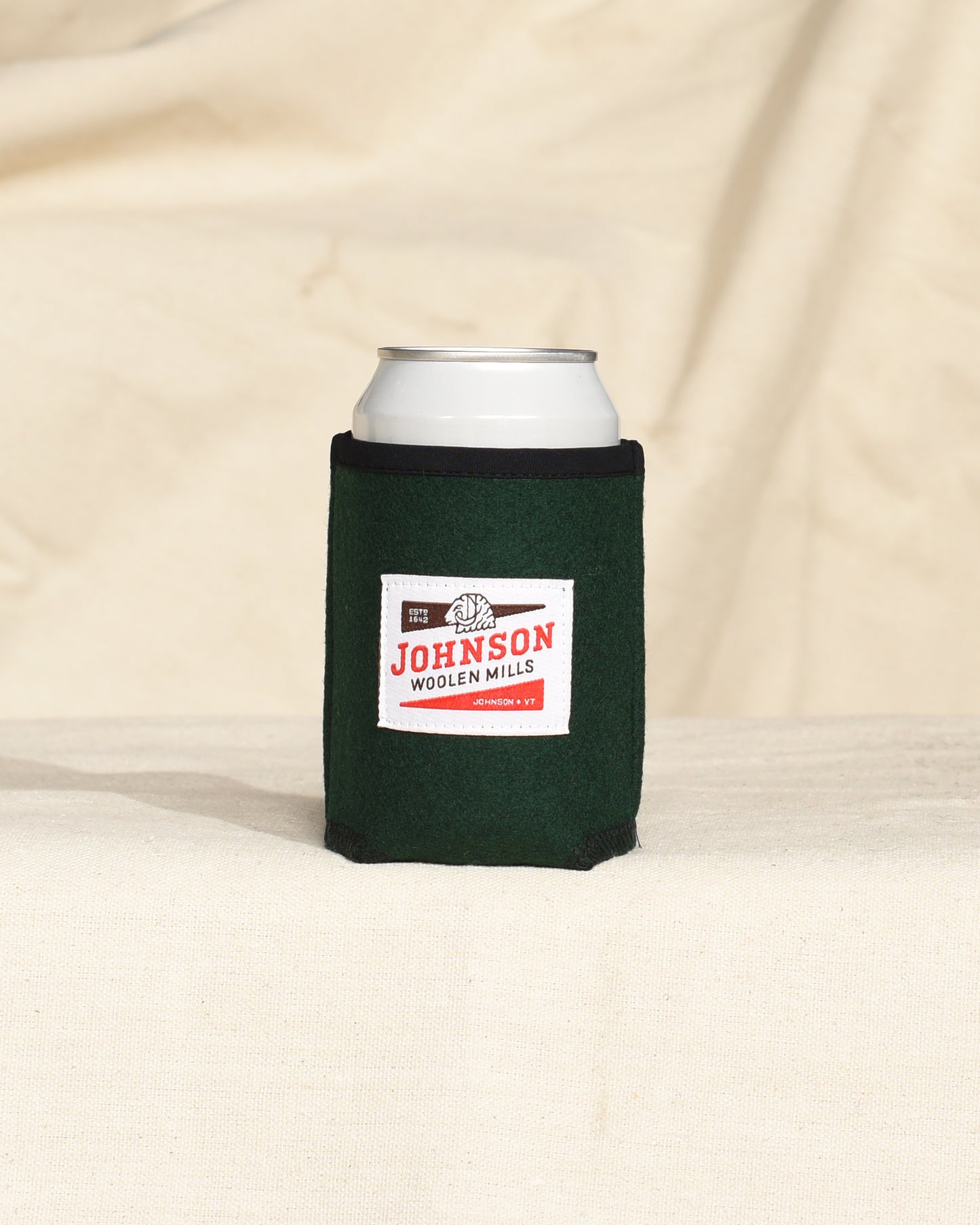 Green wool can cooler with Johnson logo on a beige surface