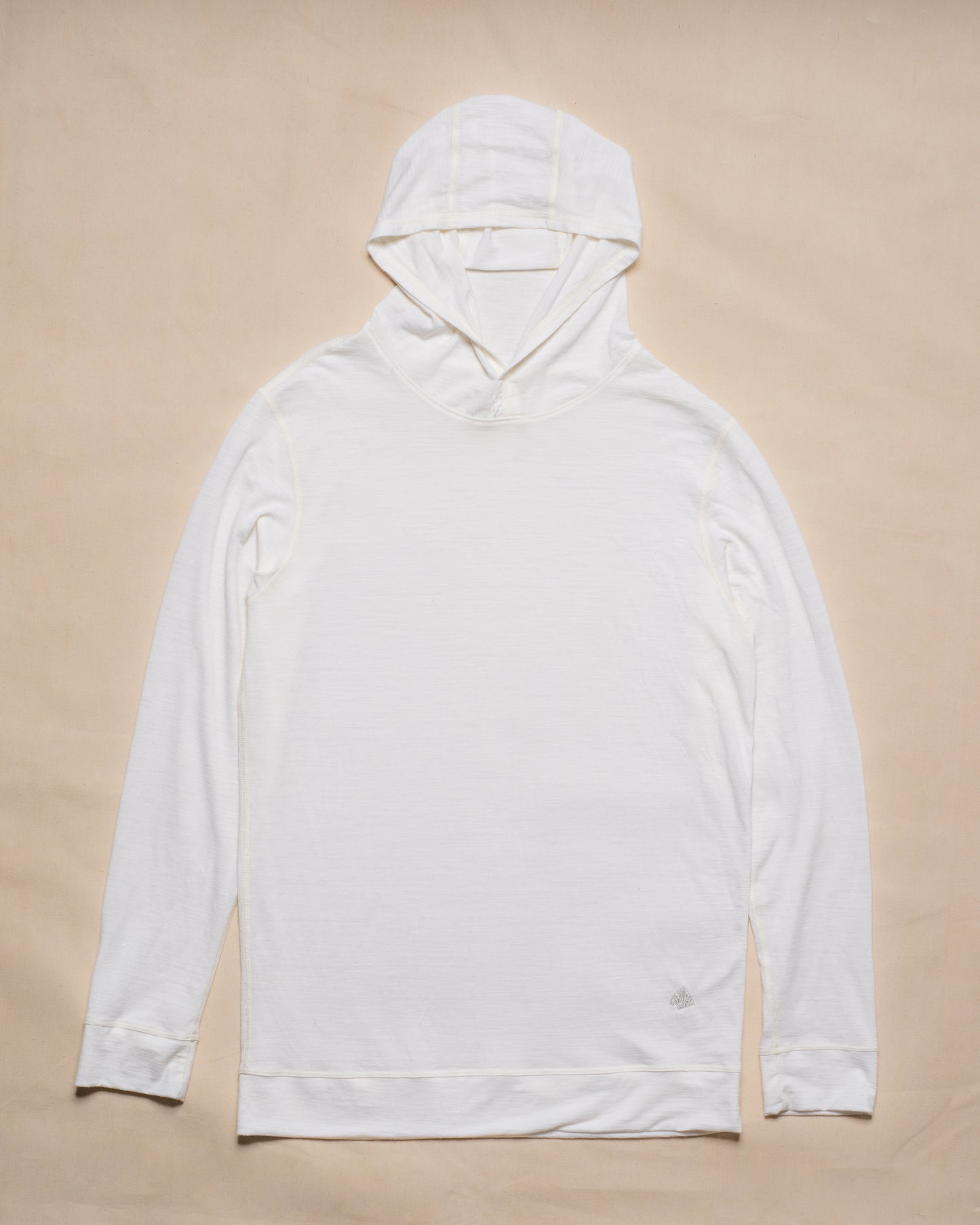A white merino wool long-sleeve hooded top laid flat on a light beige background.