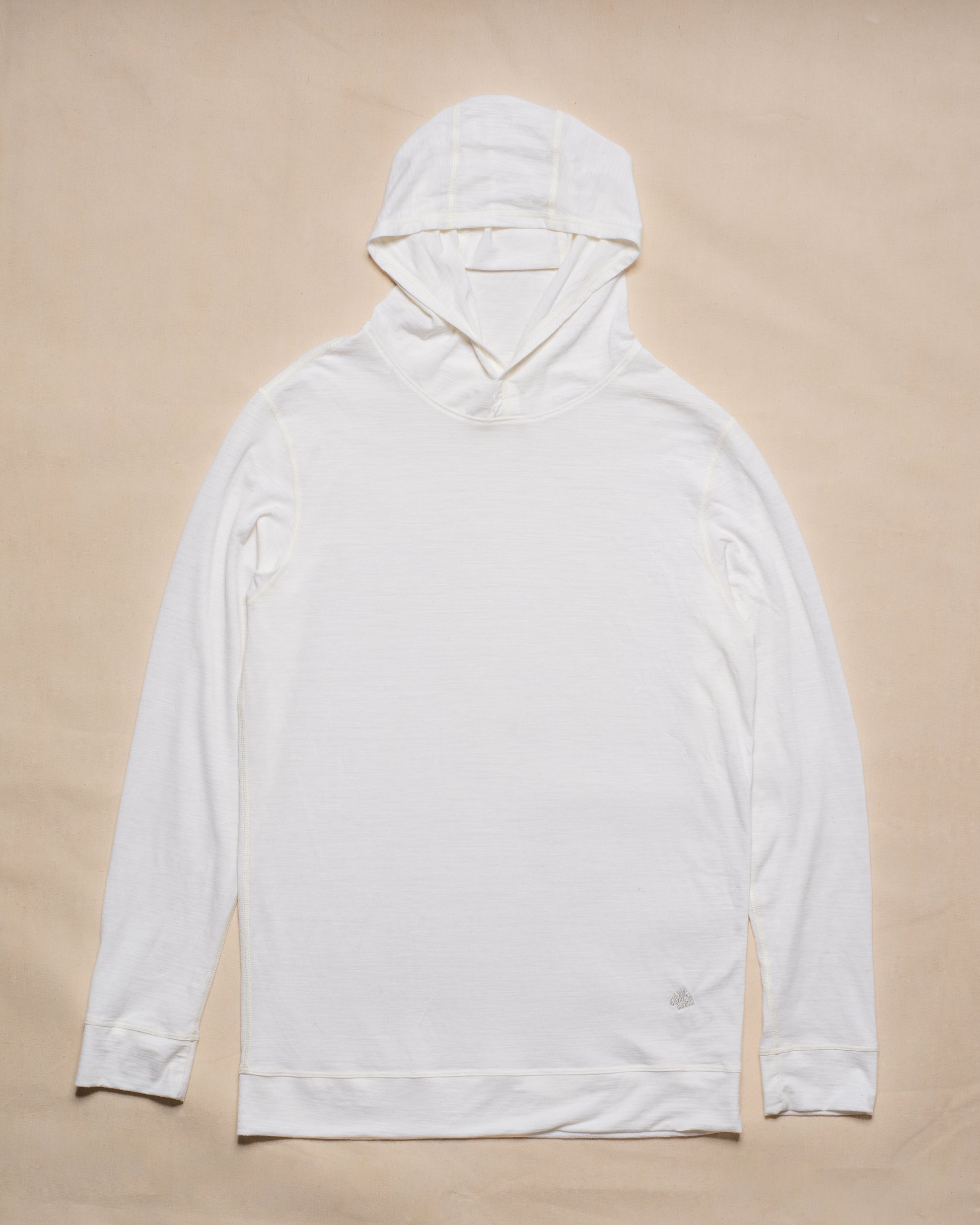 A white merino wool long-sleeve hooded top laid flat on a light beige background.
