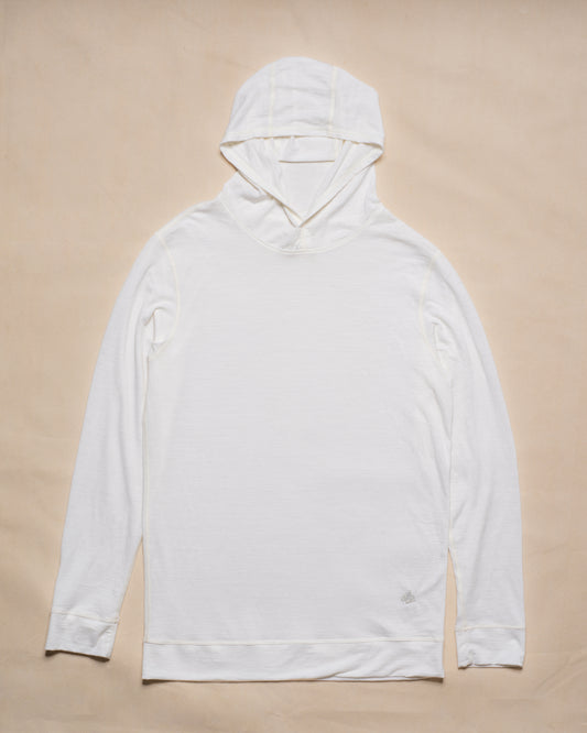 A white merino wool long-sleeve hooded top laid flat on a light beige background.