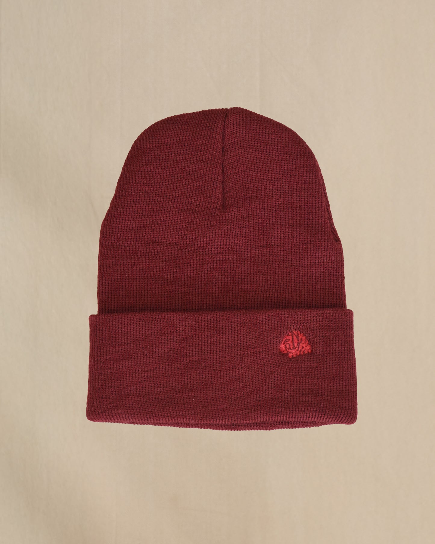 Maroon merino wool beanie with a embroidered sheep on a beige background