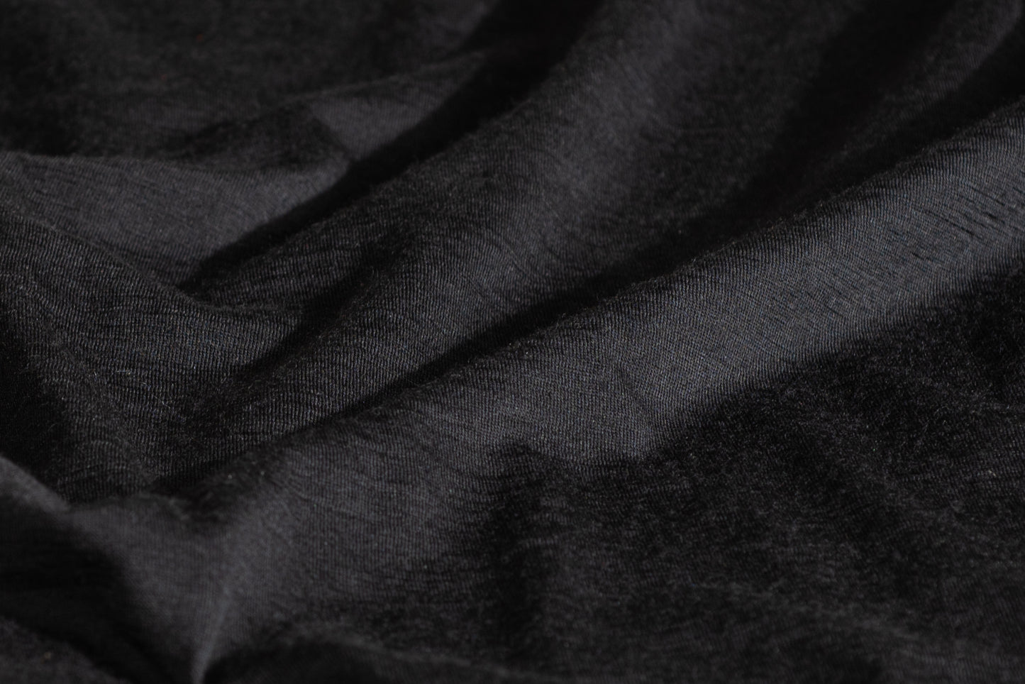 A close-up of draped black merino wool fabric with a soft, slightly textured surface.