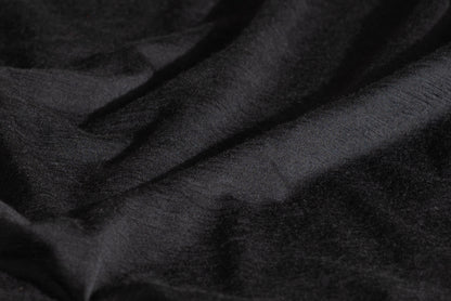 A close-up of draped black merino wool fabric with a soft, slightly textured surface.