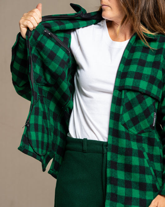 Person wearing a green and black checkered jacket over a white shirt and dark pants on a beige background