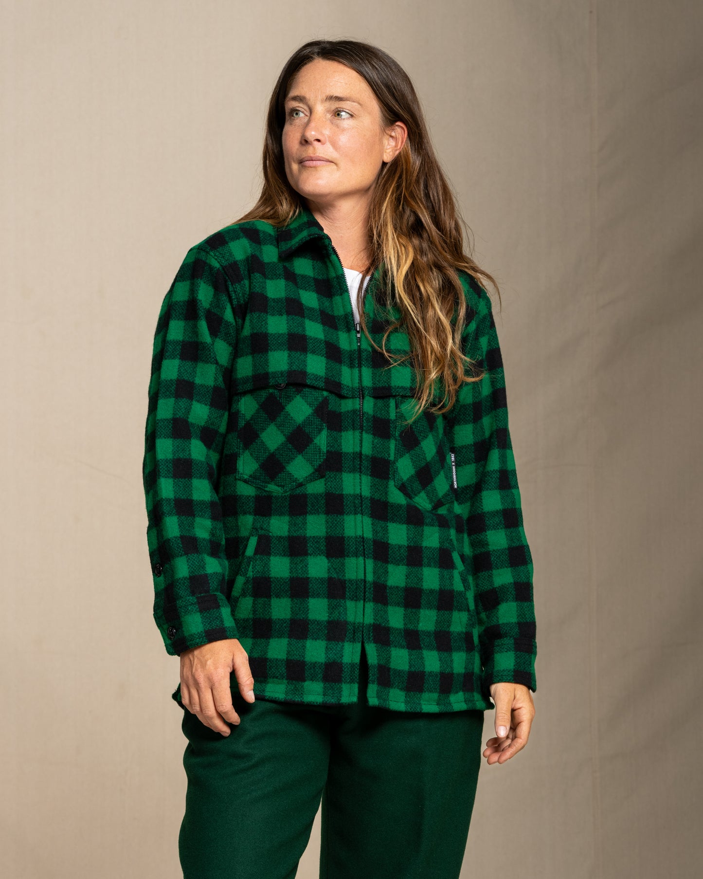 Woman wearing a green and black checkered wool jac shirt against a beige background