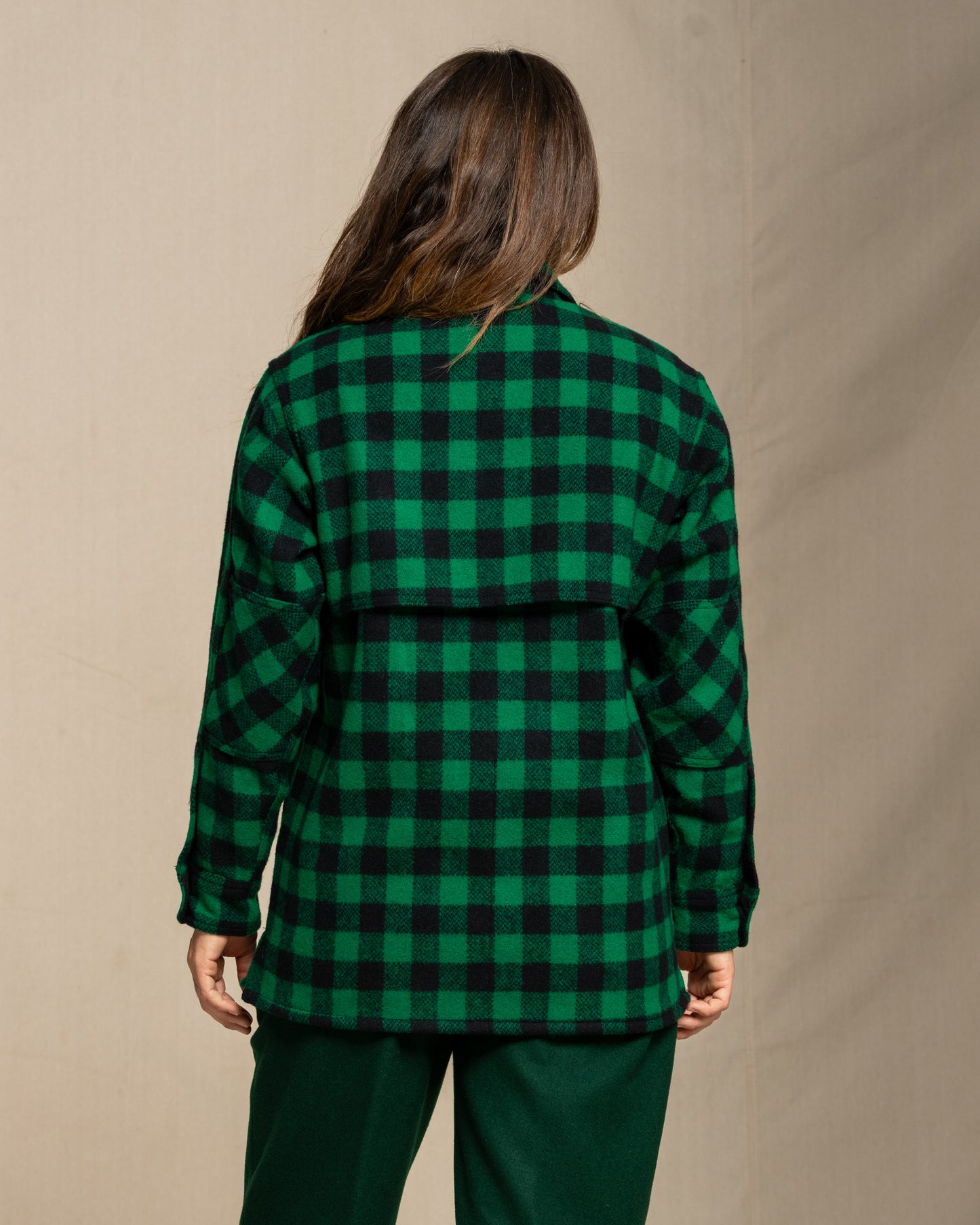 Woman wearing a green and black checkered wool jac shirt against a beige background