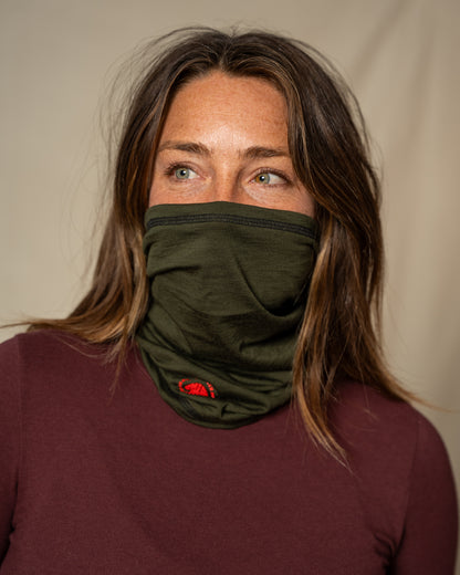 Person wearing a green merino wool neck gaiter against a beige background
