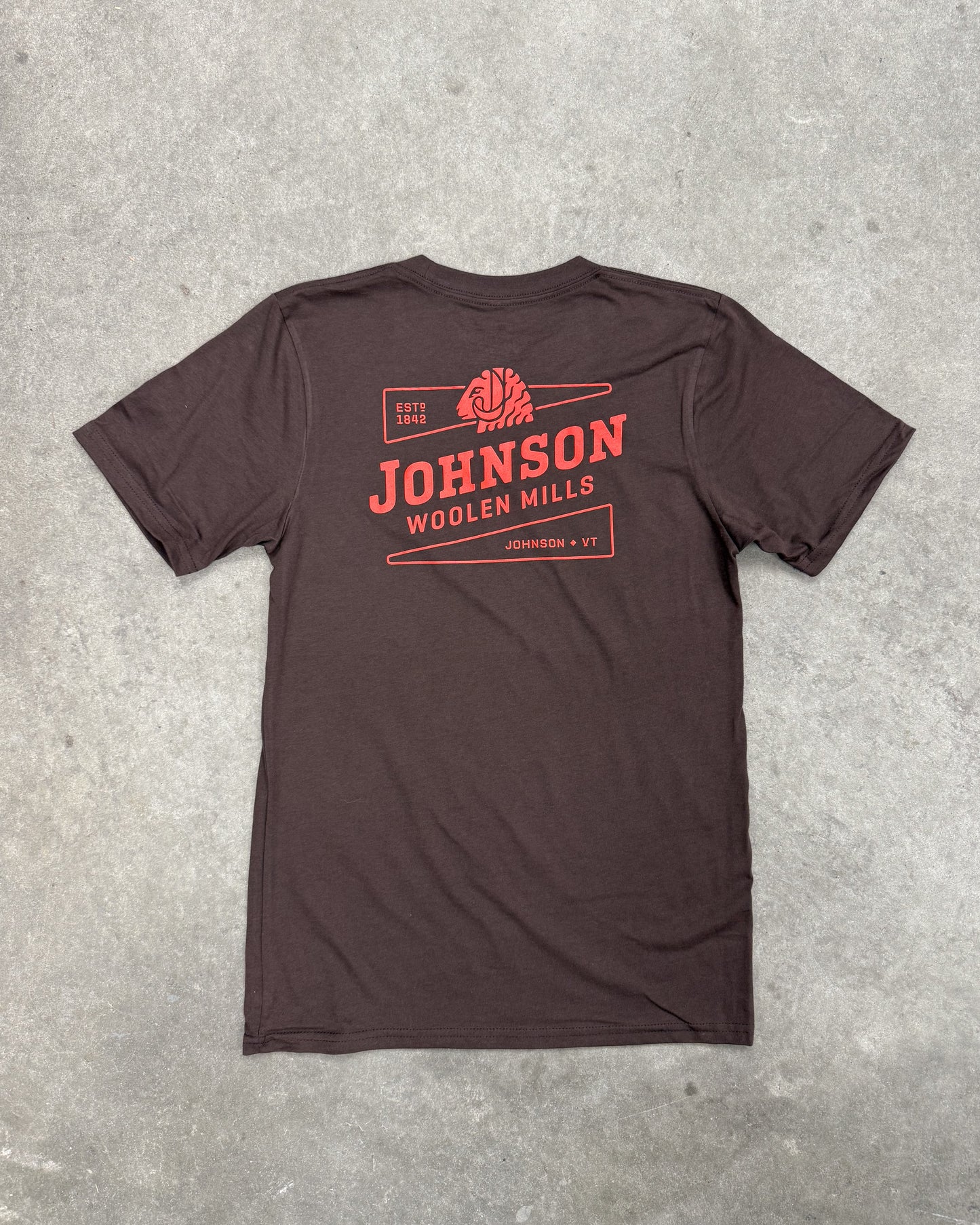 Brown t-shirt with red 'Johnson Woolen Mills' logo on a gray concrete surface