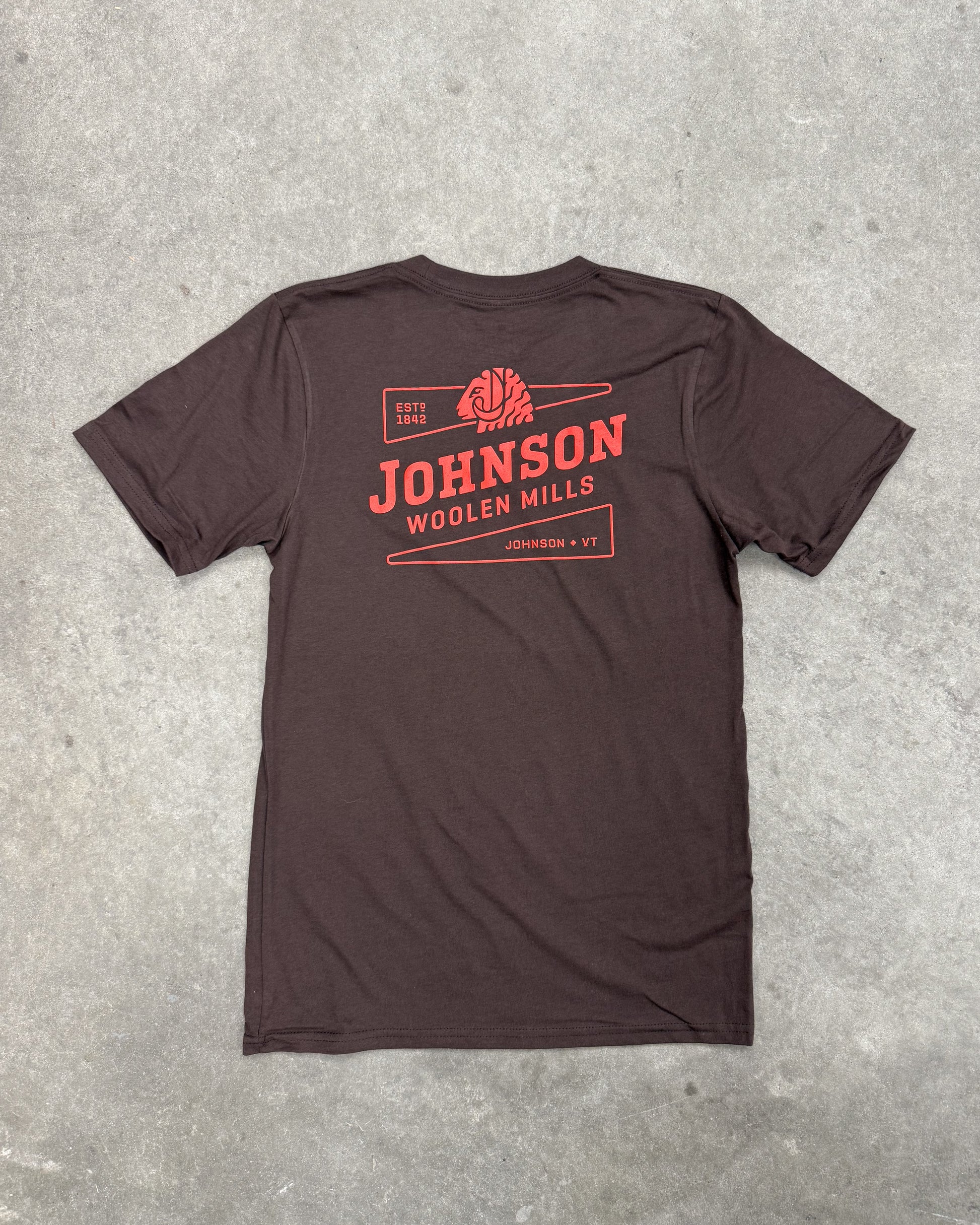 Brown t-shirt with red 'Johnson Woolen Mills' logo on a gray concrete surface