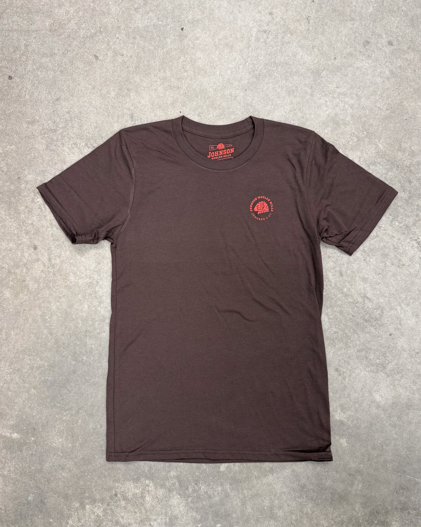 Brown t-shirt with a red logo on a gray concrete surface