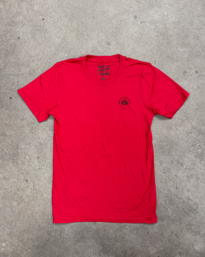 Red t-shirt with a small logo on a gray concrete surface