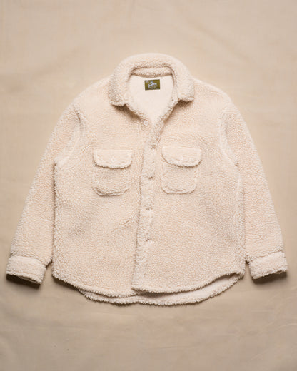 A cream-colored sherpa fleece button-up shirt jacket with two front flap pockets, laid flat on a beige fabric background.