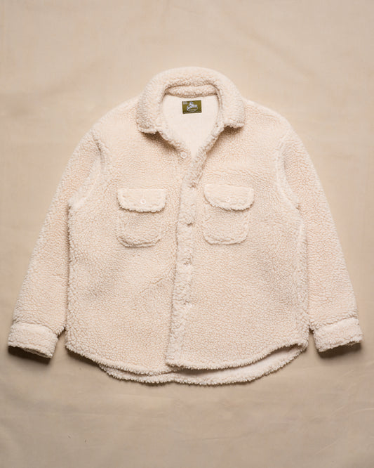 A cream-colored sherpa fleece button-up shirt jacket with two front flap pockets, laid flat on a beige fabric background.